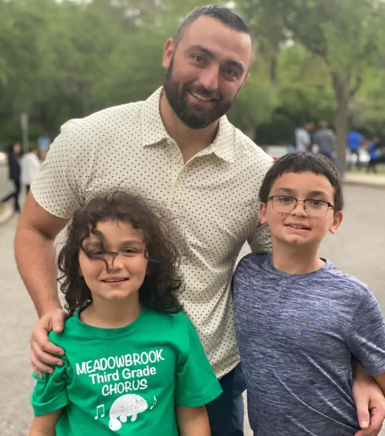 An adult, possibly a personal trainer, stands outdoors with two children—one in glasses, the other wearing a green "Meadowbrook Third Grade Chorus" shirt. Trees and people can be seen in the background.