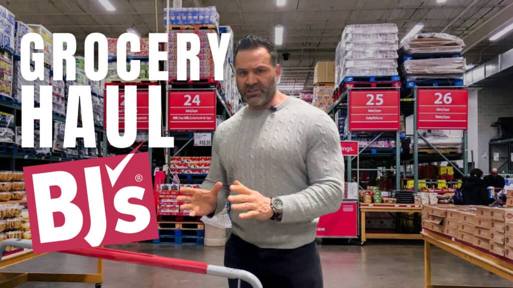 A man in a gray sweater stands in BJ’s Wholesale Club with shelves of products behind him. Large text reads "Grocery Haul BJ's"—perfect for anyone, including an online fitness coach looking for healthy meal inspirations.