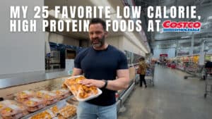 A man stands in a Costco aisle holding a food container, with text reading "My 25 favorite low calorie, high protein foods at Costco Wholesale—perfect picks for any online fitness coach or workout routine.