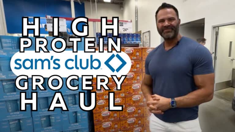 A man stands in front of stacked groceries at Sam’s Club with text overlaid reading "High Protein Sam’s Club Grocery Haul," perfect for anyone training or guided by an online fitness coach.
