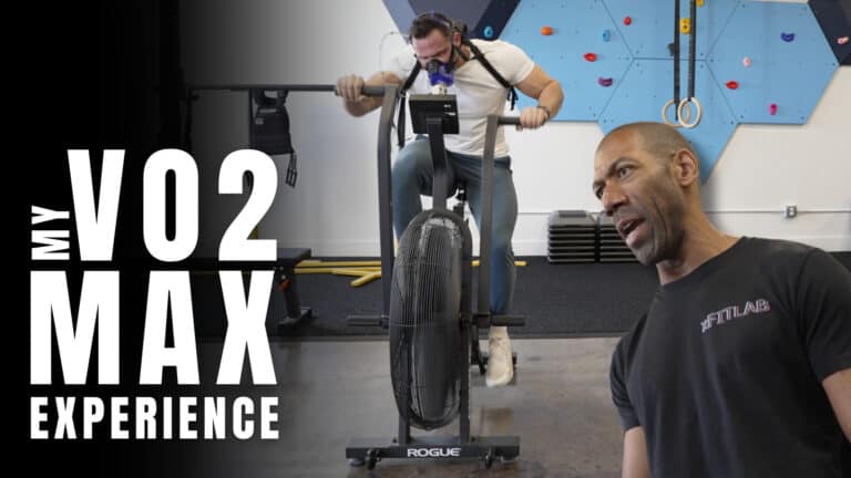 A man rides an air bike while wearing a VO2 max mask as part of his training; another man, possibly a personal trainer, stands in the foreground. Large text reads "My VO2 Max Experience.