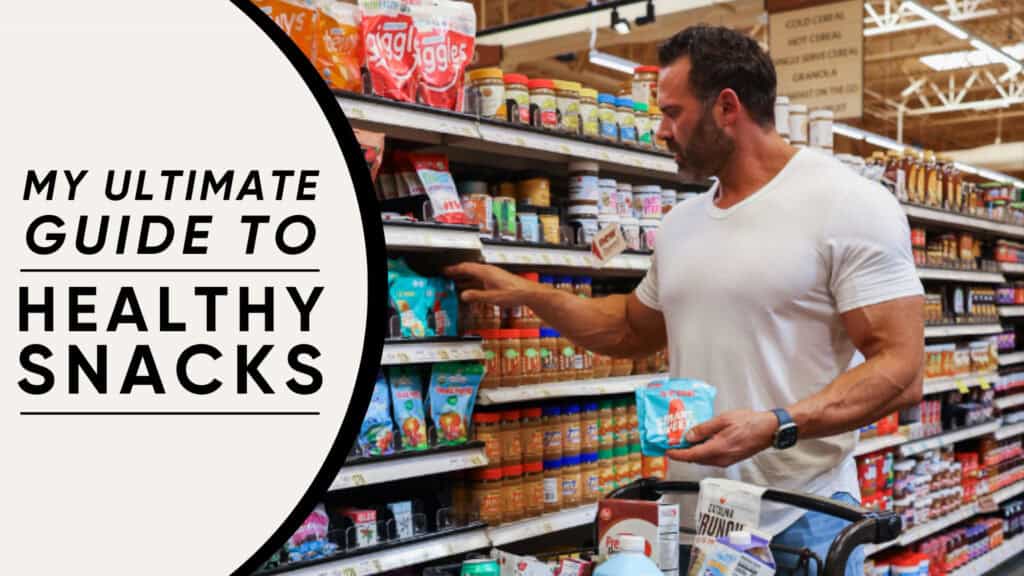 A man in a grocery store selects healthy snacks from a shelf, holding a shopping basket with various items. Text on the left reads: "My Ultimate Guide to Healthy Snacks by your online fitness coach.