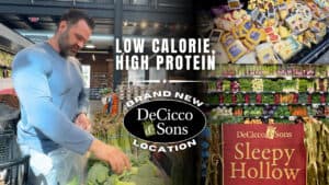 A man shops for vegetables at DeCicco & Sons; displays of cheese, produce, and a "Sleepy Hollow" sign promote the brand's new location with "Low Calorie, High Protein" text for added nutrition.